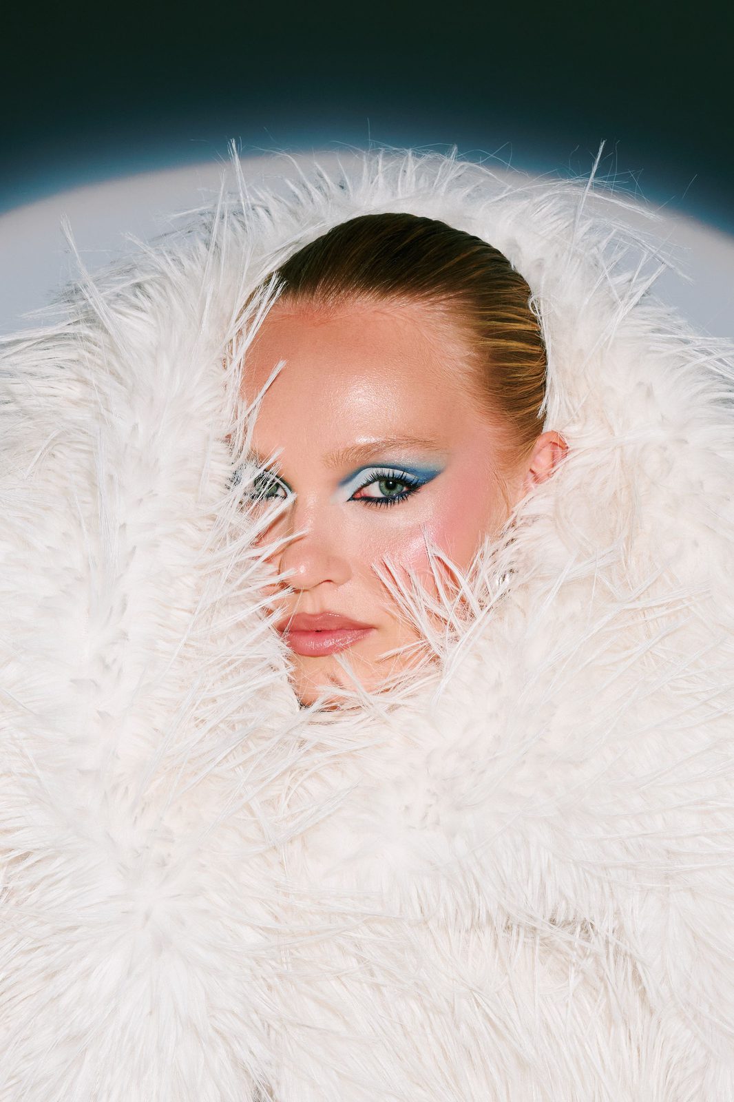 Teal graphic liner framed by white feathers, beauty editorial by Andrada Rusu